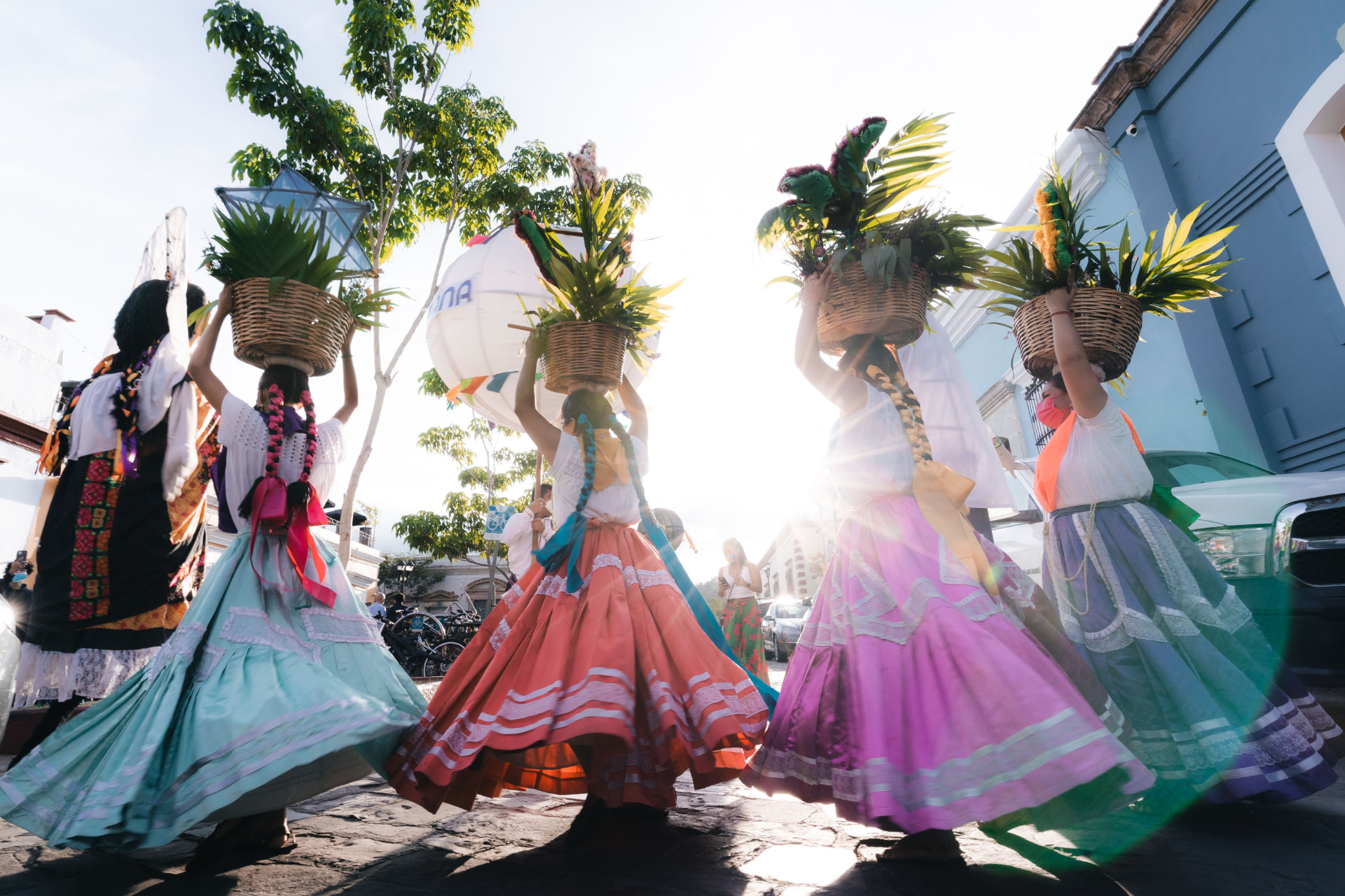 Dancers in colorful traditional skirts carrying woven baskets of flowers and palm on their heads during a festive procession