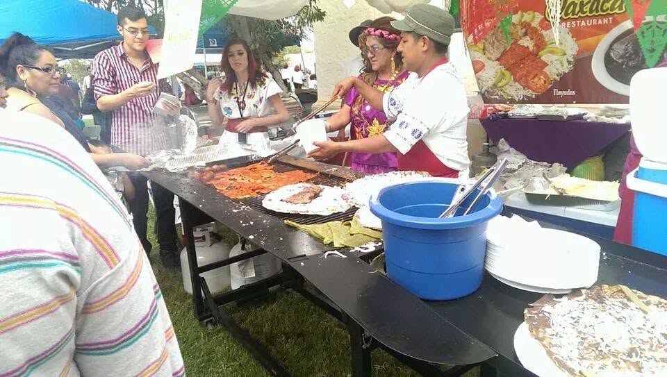 Women in traditional dress grilling tlayudas at an outdoor cookout, with Tomasa serving guests