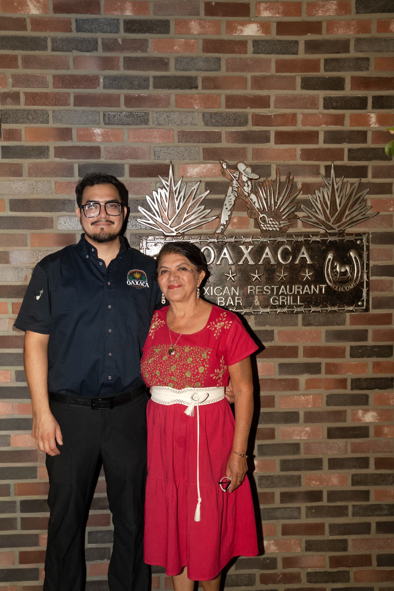 Two members of the Oaxaca family standing together in front of the restaurant's agave-crest sign