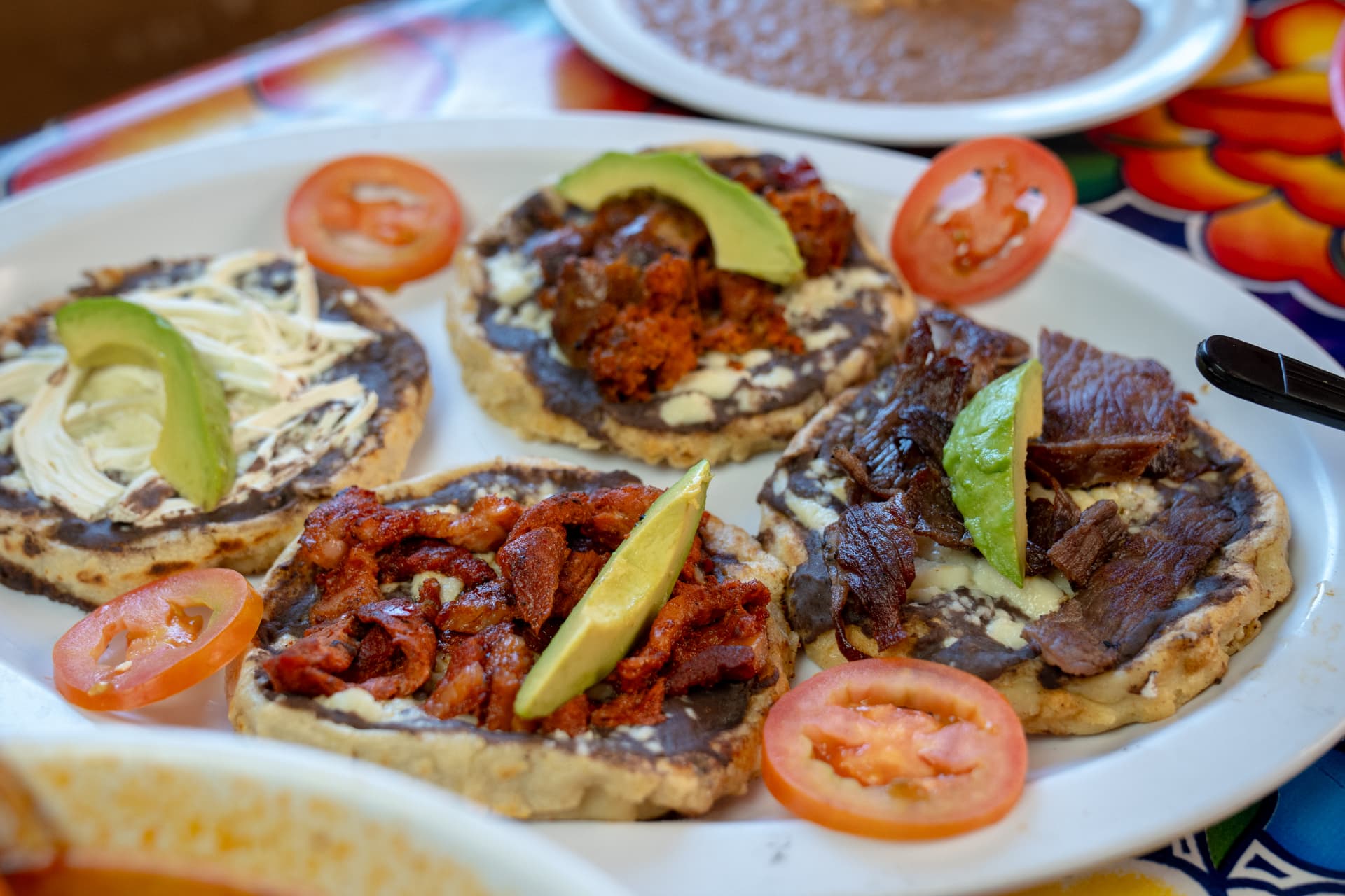 A plate of memelas with black beans, avocado, and salsa roja